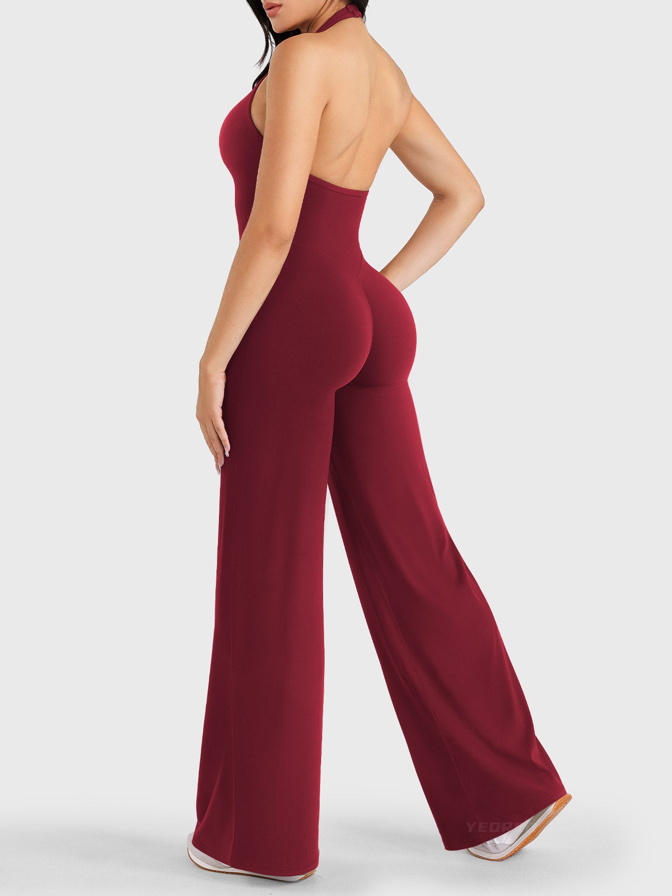 Walking side-back view showing anchor red halter open-back jumpsuit with V-back shaping