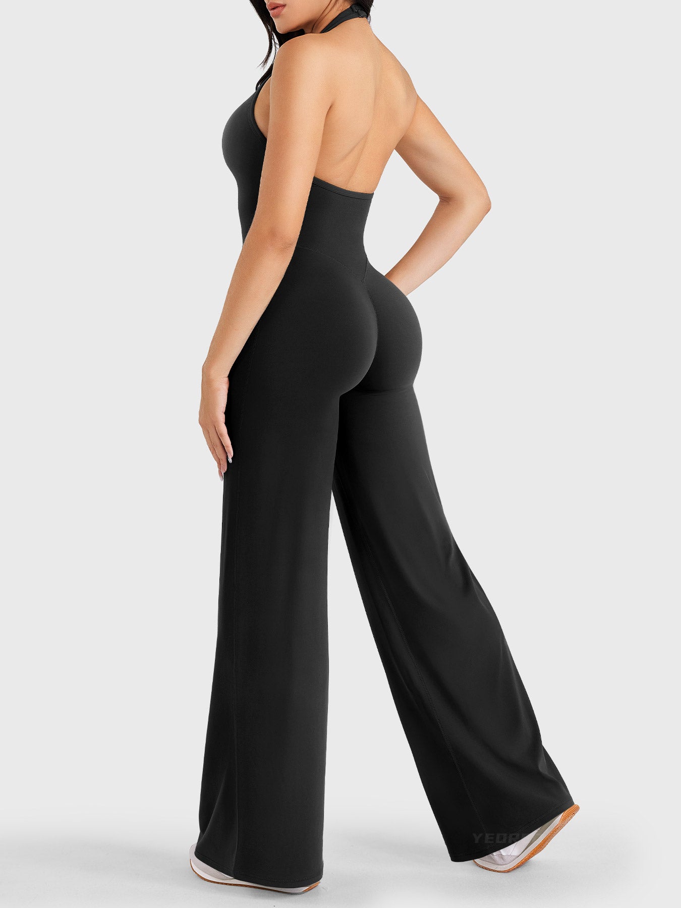 Walking side-back view showing black halter open-back jumpsuit with V-back shaping