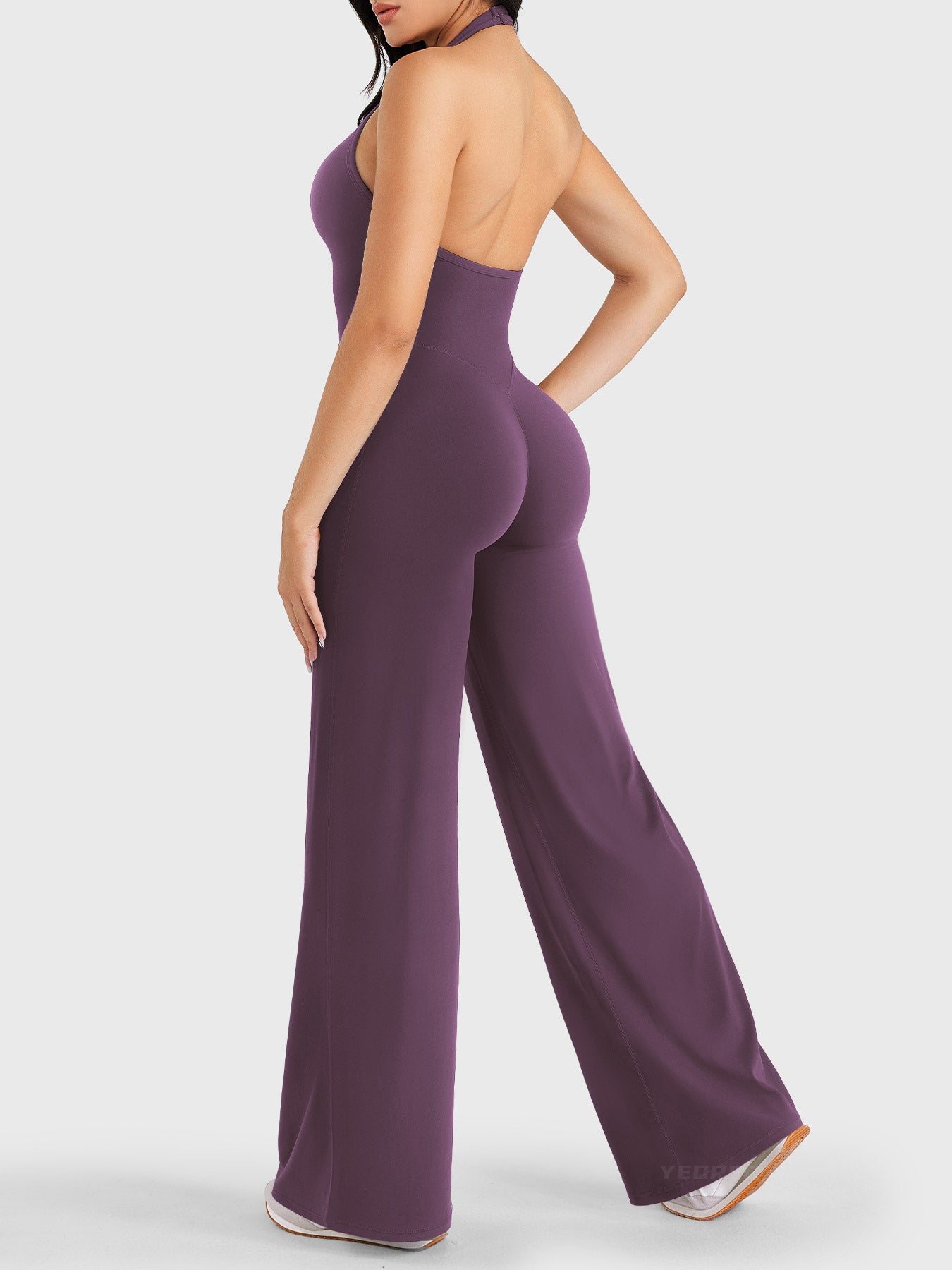 Walking side-back view showing black berry halter open-back jumpsuit with V-back shaping