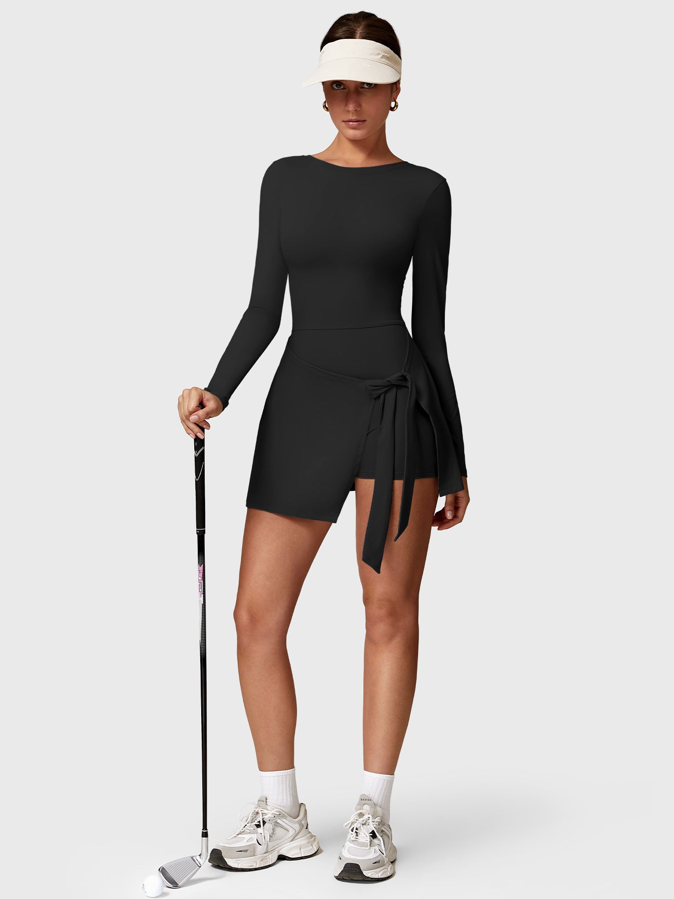 Lifestyle shot front view of Yeoreo Renee Long Sleeve Tennis Dress in Black – model holding a golf club, ready to play