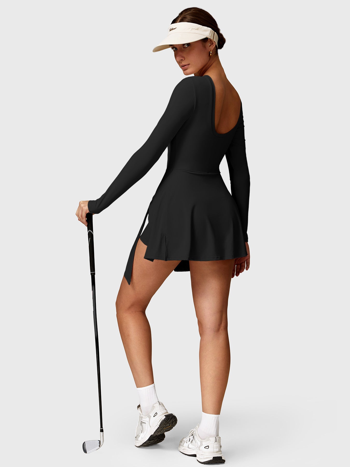 Lifestyle shot back view of Yeoreo Renee Long Sleeve Tennis Dress in Black – model holding a golf club, ready to play