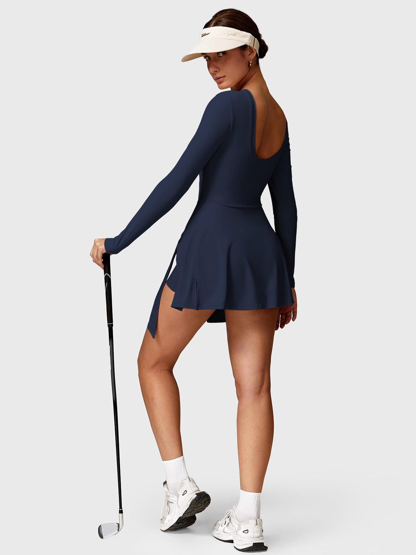 Lifestyle shot front view of Yeoreo Renee Long Sleeve Tennis Dress in deep blue – model holding a golf club, ready to play