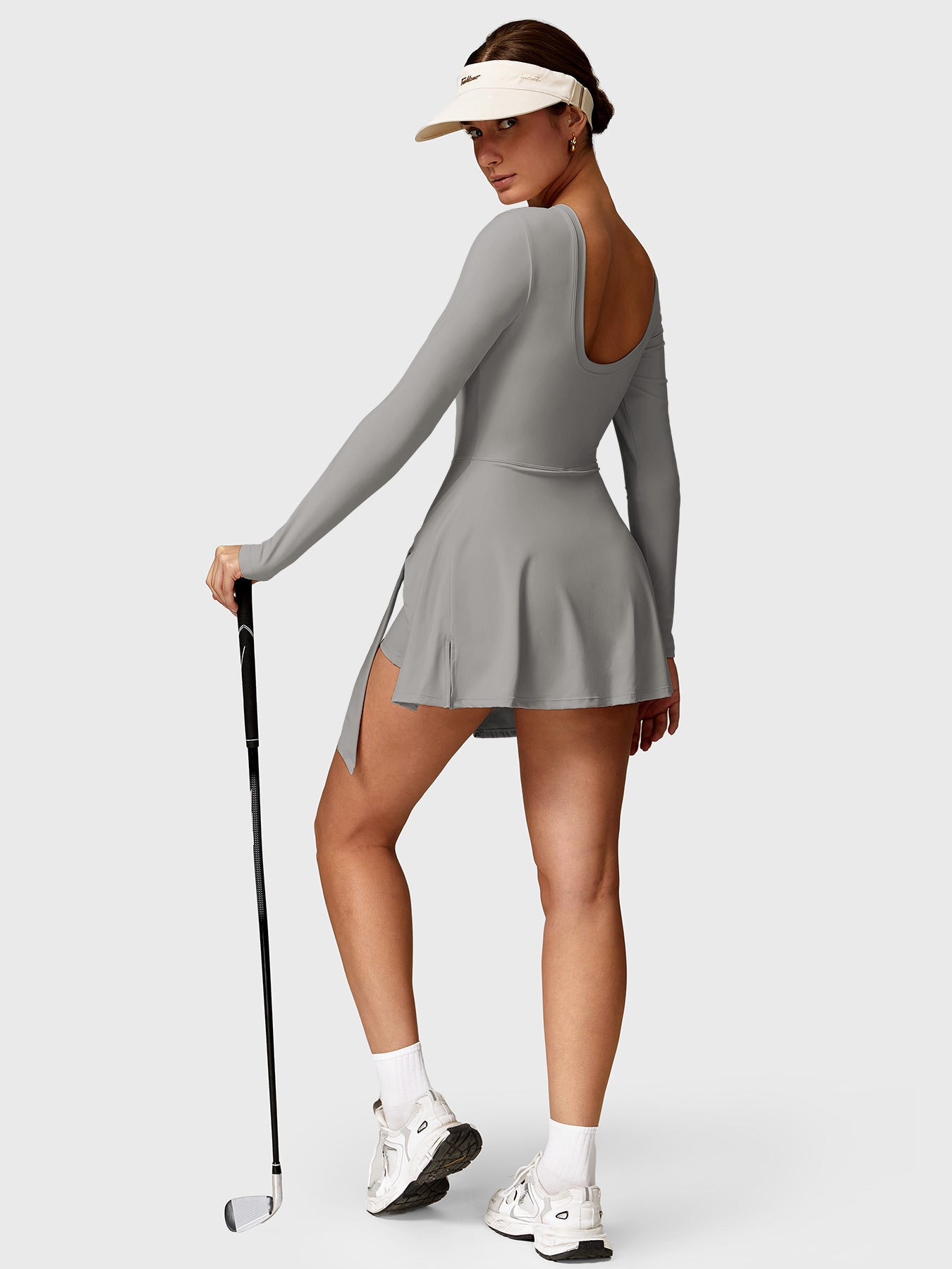 Lifestyle shot back view of Yeoreo Renee Long Sleeve Tennis Dress in grey – model holding a golf club, ready to play