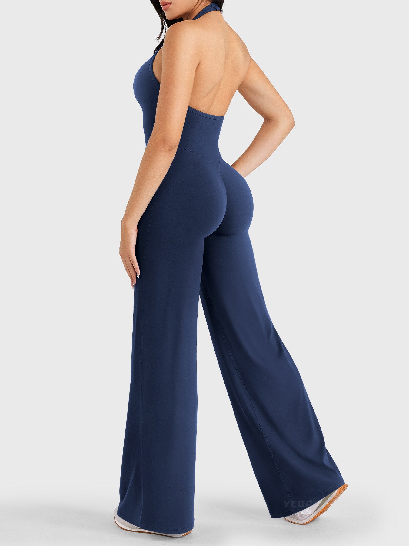 Walking side-back view showing navy halter open-back jumpsuit with V-back shaping