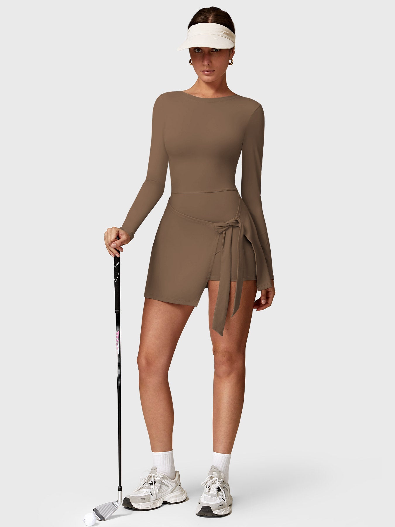 Lifestyle shot front view of Yeoreo Renee Long Sleeve Tennis Dress in brown – model holding a golf club, ready to play