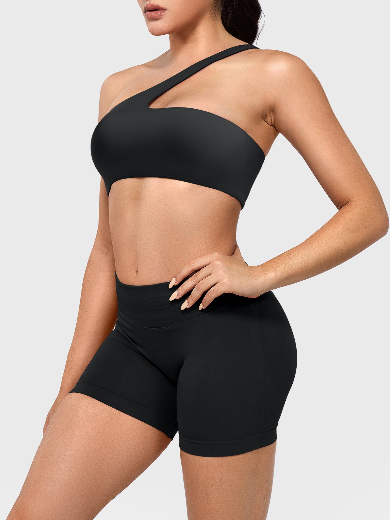 Claranie One Shoulder Sports Bra in black, angled front upper body view styled with shorts, body-contouring athletic fit
