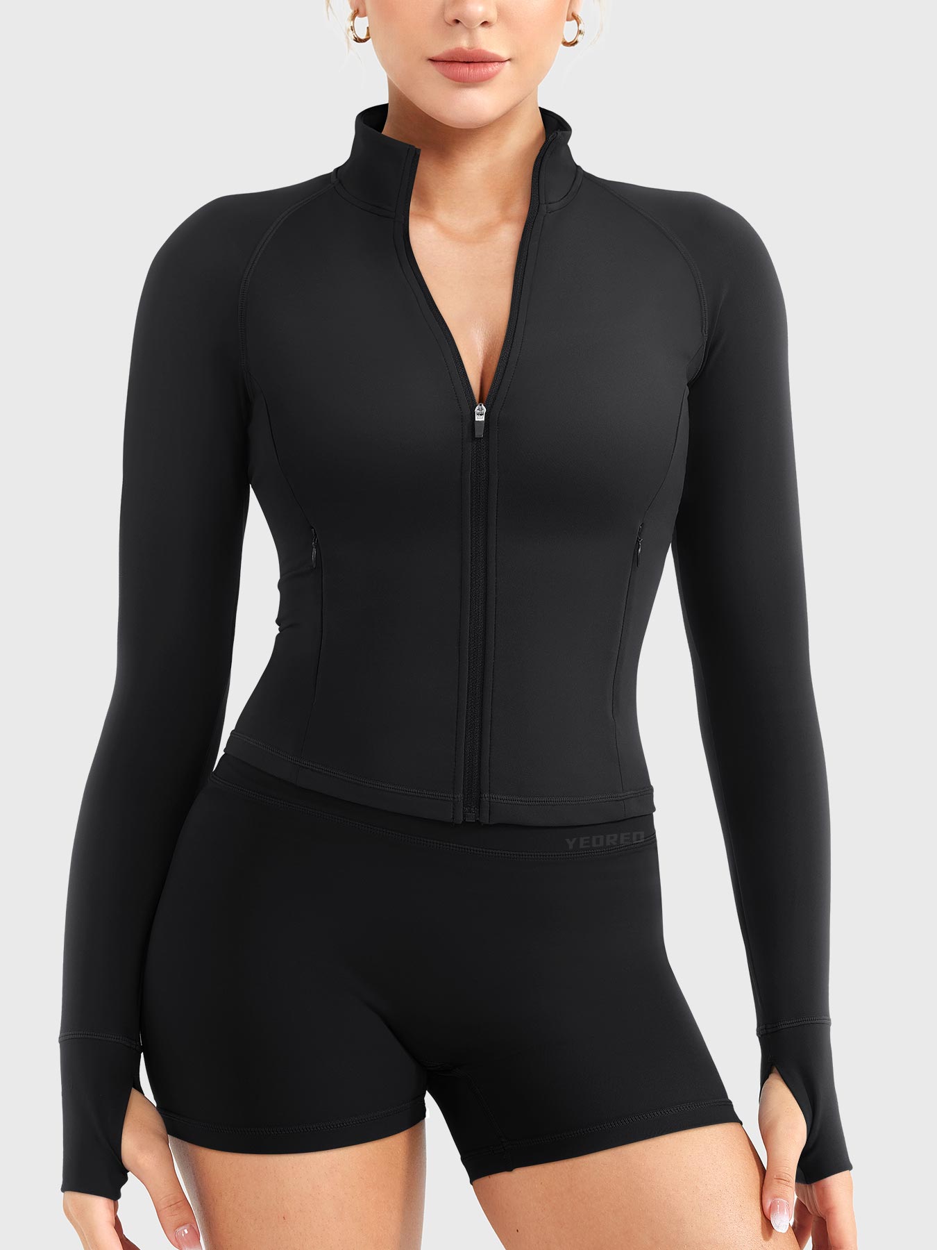 Candecy Full Zip Workout Jacket in black, front view standing, partially unzipped V neckline, princess seams, hidden zip pockets, thumbhole cuffs