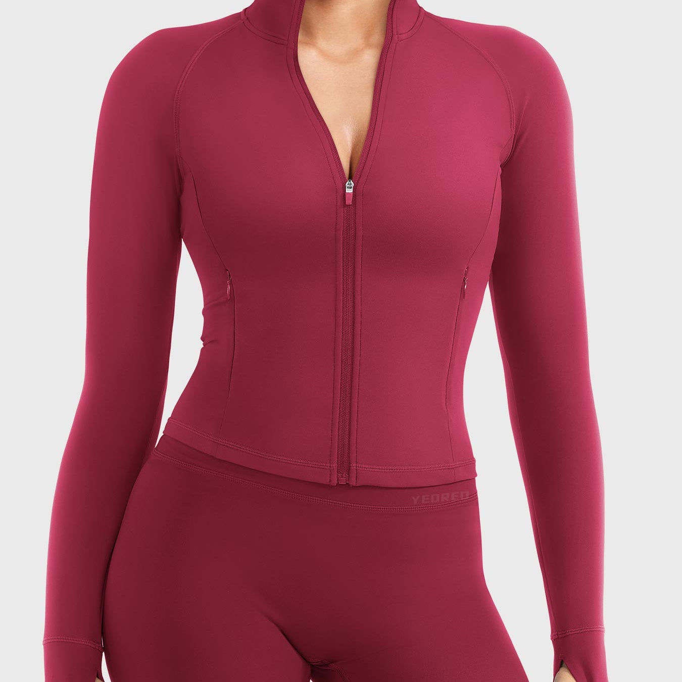 Candecy Full Zip Workout Jacket in ruby red, front view standing, partially unzipped V neckline, princess seams, hidden zip pockets, thumbhole sleeves