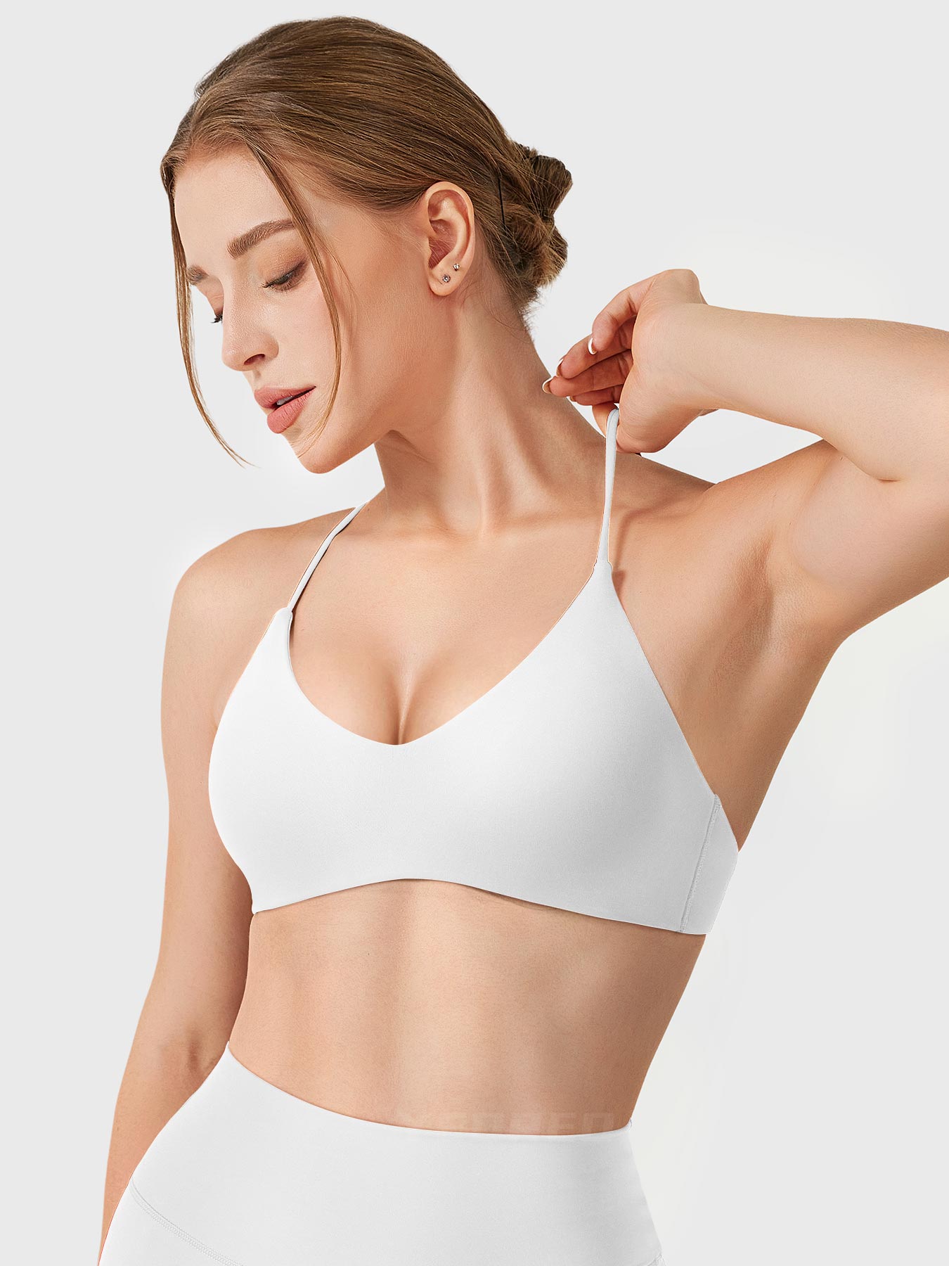 White Yeoreo Zaahira V-neck sports bra angled front view, model stretching shoulder strap to show flexibility