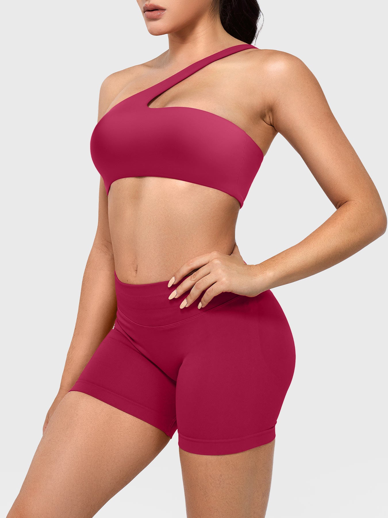 Claranie One Shoulder Sports Bra in ruby red, angled front upper body view styled with shorts, body-hugging fit highlighting curves