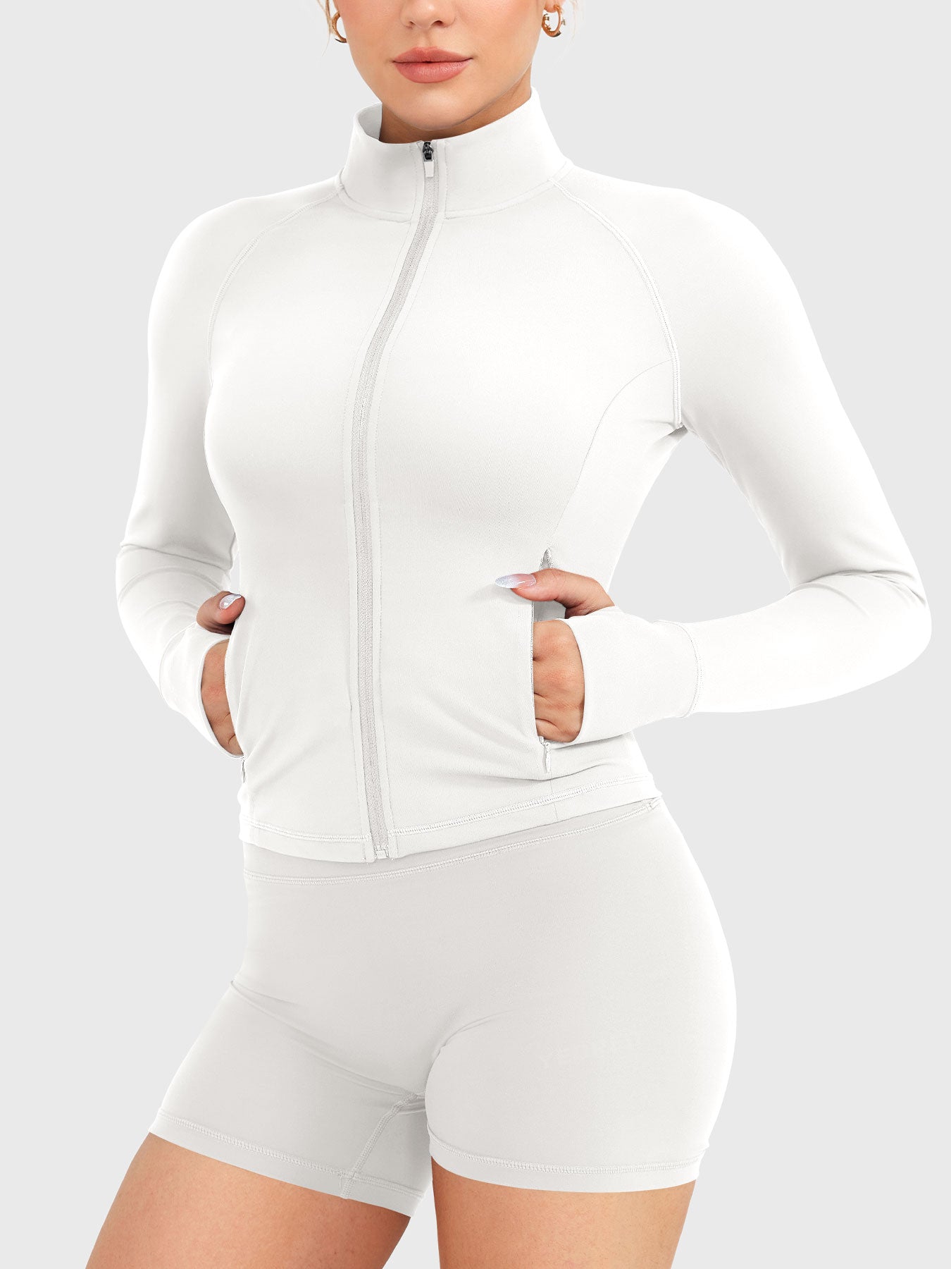 Candecy Full Zip Workout Jacket in white, angled front view with hands in pockets, fully zipped high neck, clean fitted silhouette