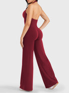 Walking side-back view showing anchor red halter open-back jumpsuit with V-back shaping
