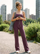 Dagyane Straight Leg Jumpsuit in black berry, model standing on street listening to music with yoga mat over shoulder, relaxed active lifestyle