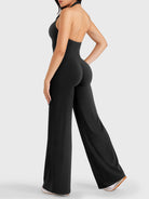 Walking side-back view showing black halter open-back jumpsuit with V-back shaping