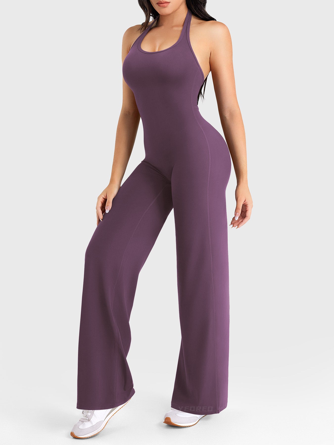 Back-angle stretch pose showing hidden-scrunch booty lift in black berry halter jumpsuit