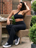 Claranie One Shoulder Sports Bra in black, outdoor cafe scene with model seated at table, styled with straight leg pants, elegant and relaxed look