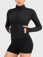 Candecy Full Zip Workout Jacket in black, angled front pose with hands in pockets, fully zipped high neck, slim and sculpted silhouette