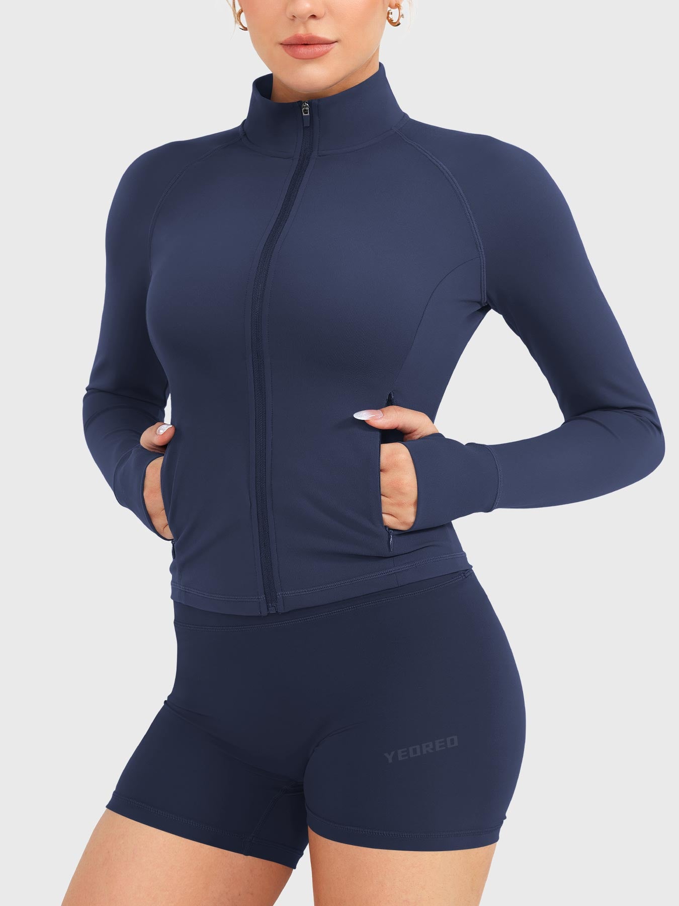 Candecy Full Zip Workout Jacket in navy, angled front view with hands in pockets, fully zipped high neck, fitted activewear look