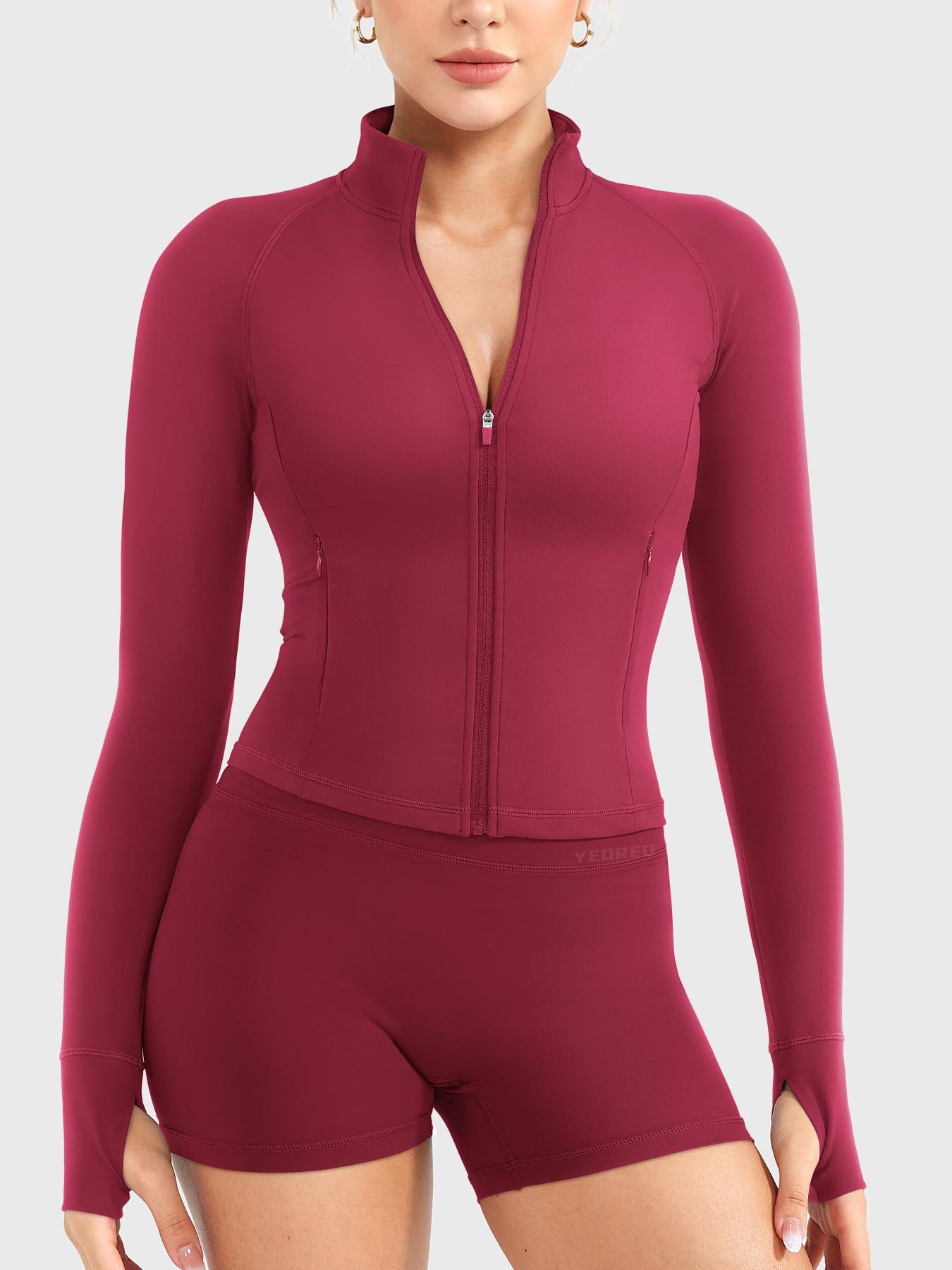 Candecy Full Zip Workout Jacket in ruby red, front view standing, partially unzipped V neckline, princess seams, hidden zip pockets, thumbhole sleeves