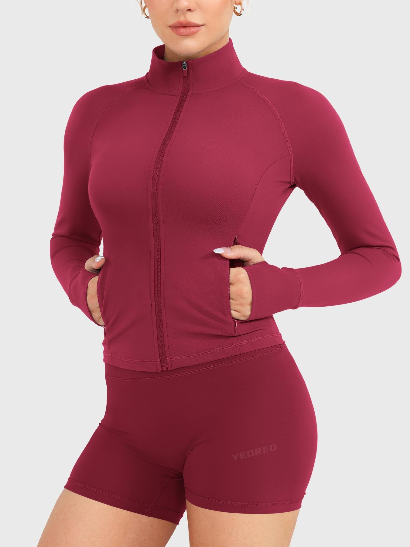Candecy Full Zip Workout Jacket in ruby red, angled front pose with hands in pockets, fully zipped high neck, sculpted fit