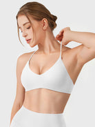 White Yeoreo Zaahira V-neck sports bra angled front view, model stretching shoulder strap to show flexibility