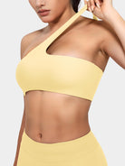 Claranie One Shoulder Sports Bra in milk yellow, angled front upper body view, model pulling shoulder strap to show stretch and flexibility