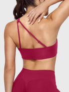Claranie One Shoulder Sports Bra in ruby red, angled back view upper body with hand on shoulder, side coverage support, elegant open back