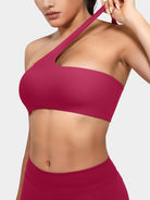 Claranie One Shoulder Sports Bra in ruby red, angled front upper body view, model stretching shoulder strap to show elasticity