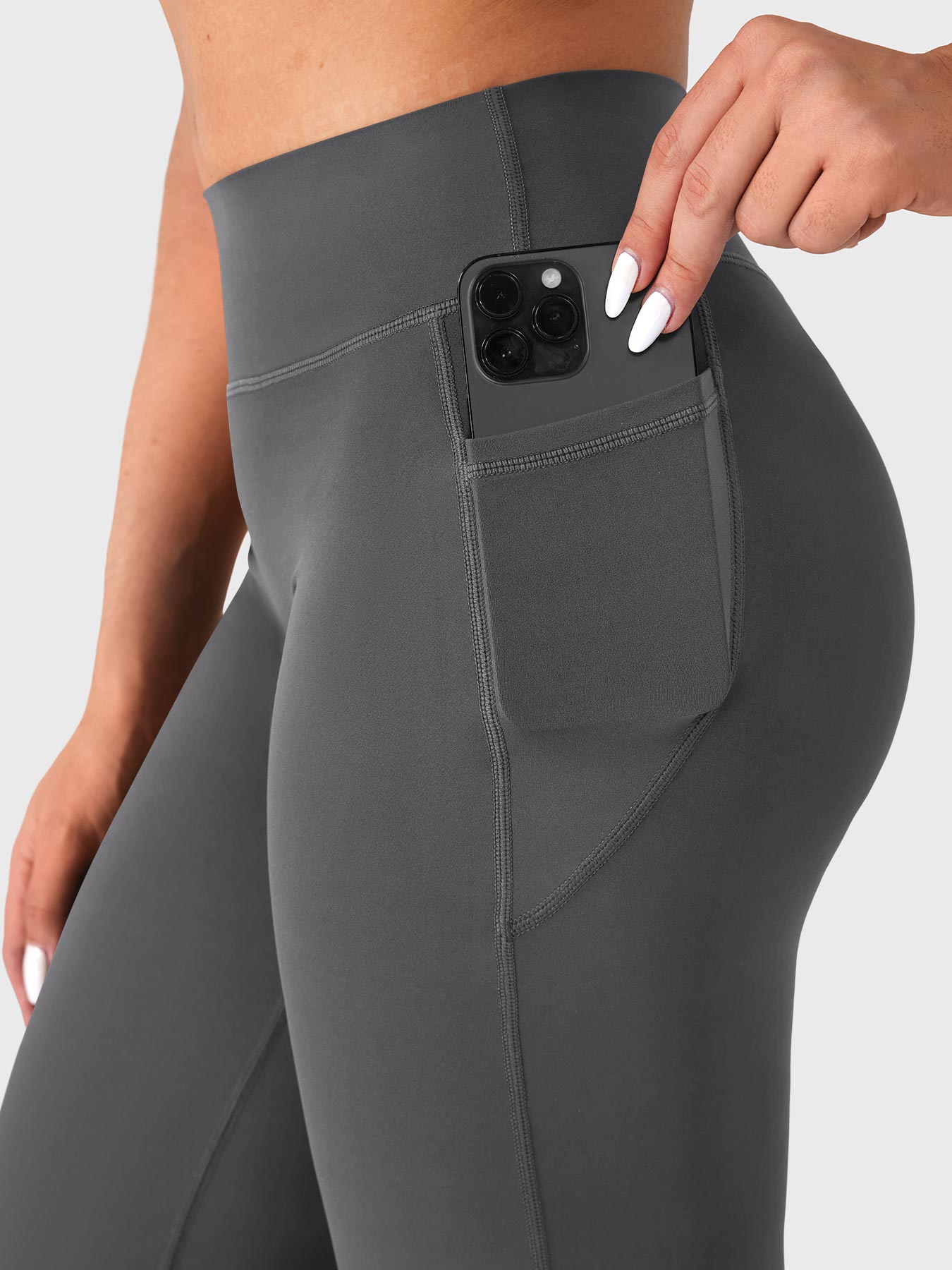 Dark grey straight leg leggings with side pockets holding a phone, functional athleisure design